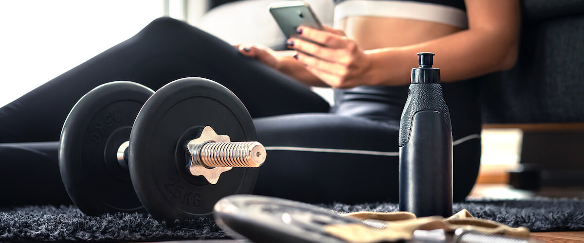 A woman exercising at home with dumbbells while checking her Evolution Nutrition at-home workout plan.